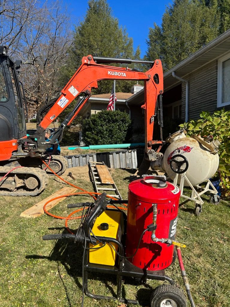 Construction site with a excavator, a red spray machine, and construction materials against a clear blue sky.