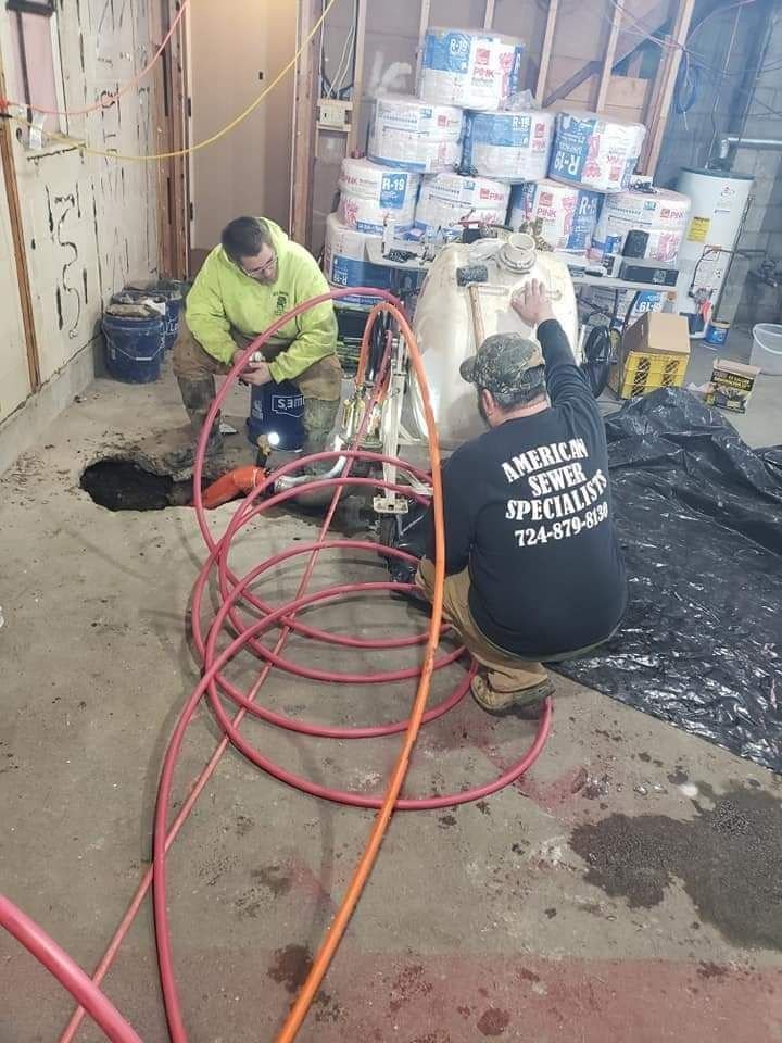 Two workers in safety attire operate a machine with colorful hoses in a construction area, surrounded by materials and tools.